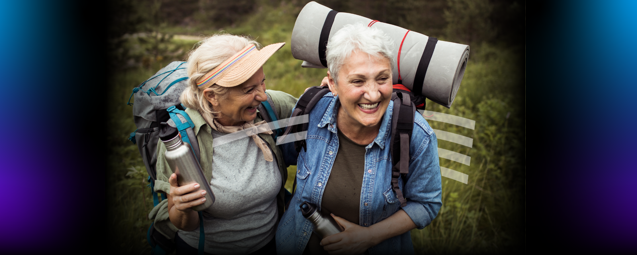 two older women laughing and hugging while hiking and carrying reusable water bottles and backpacks