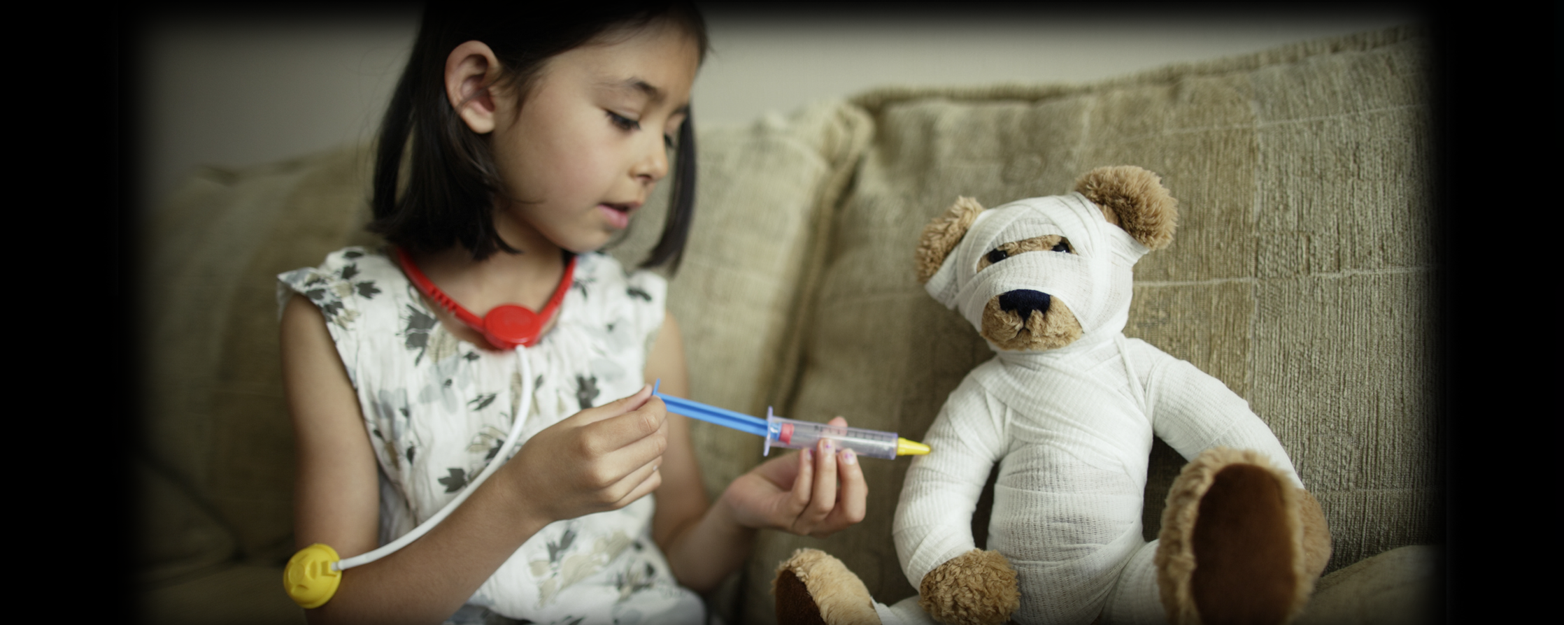 Little girl giving her teddy bear a shot