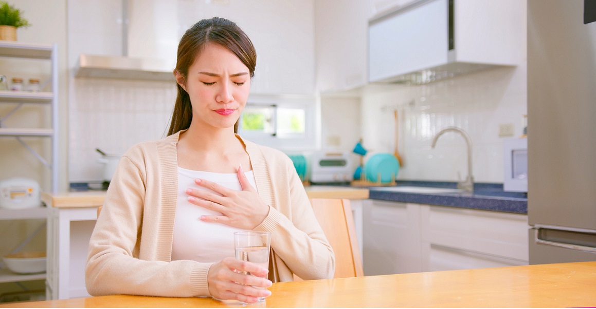 Woman holding glass of water with one hand and one hand at heart