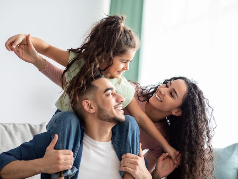 Portraif Of Cheerful Middle Eastern Family Of Three Having Fun Together At Home. Young Arabic Parents Playing With Their Little Daughter In Living Room, Mom, Dad And Child Smiling And Laughing