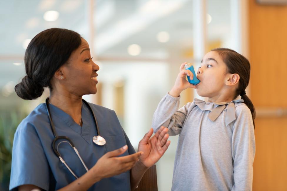 Smiling nurse cheering on little girl using an inhaler