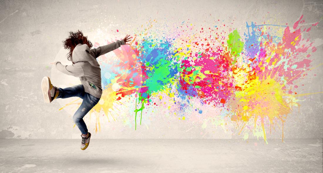 A person kicking one foot in the air with a colorful paint splatter on the wall behind them