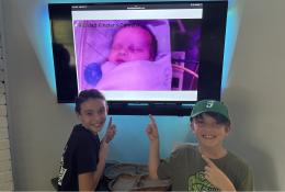 Two young boys watching their new baby brother on digital screen at home