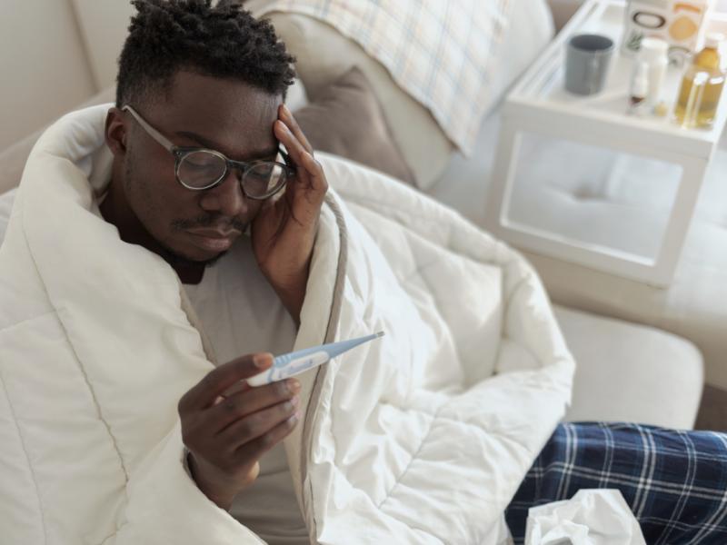 man covered in blanket and checking fever in thermostat 