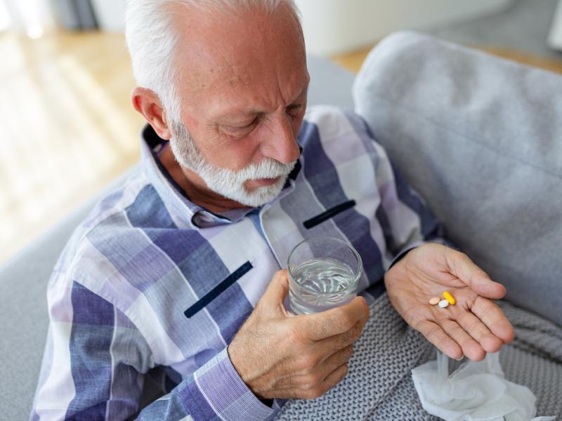 Man taking medicines and holding glass of water in another hand