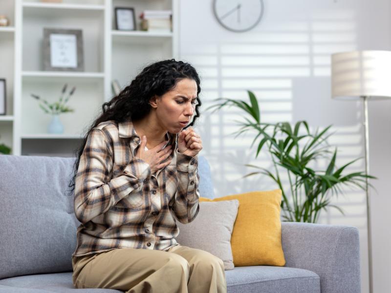 Woman sitting on couch and coughing