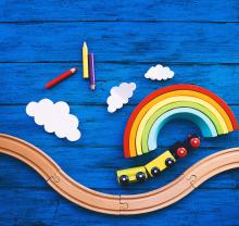 Wooden toy train, railway for preschool child, wood rainbow, colored pencils on blue table. Daycare, kindergarten or montessori school background. Kids dream, Learn and Play concept